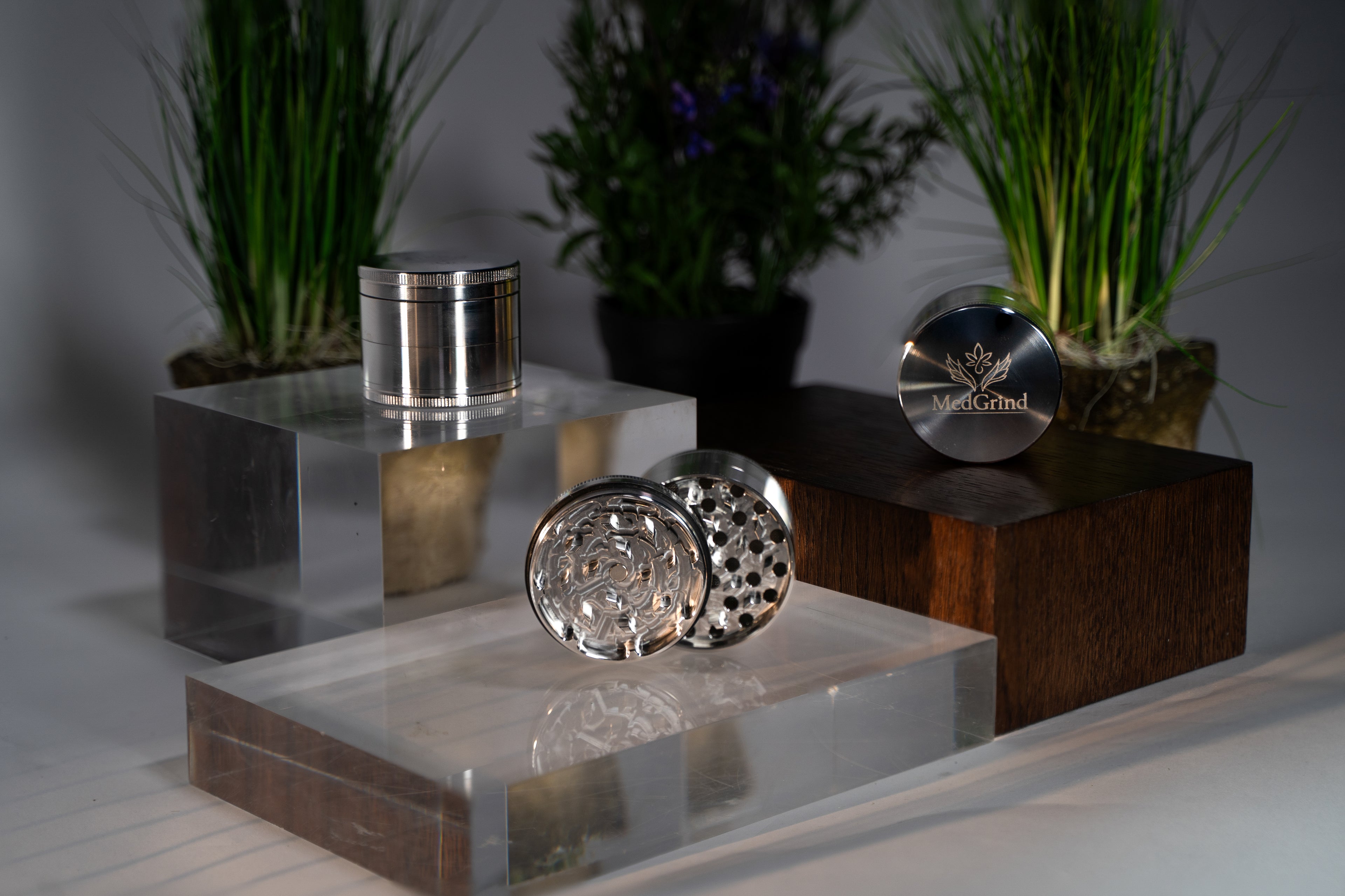MedGrind Premium Edelstahl Grinder 63 mm – passivierter Edelstahl 304, rostfrei und langlebig, geöffnet mit Mahlwerk und geschlossen, präsentiert auf Acryl- und Holzpodesten